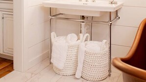 Un baño con un lavabo blanco, un espejo con luces y dos cestas blancas.