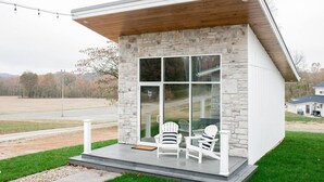 Una casa moderna con fachada de piedra, ventanas grandes y un porche con dos sillas Adirondack.