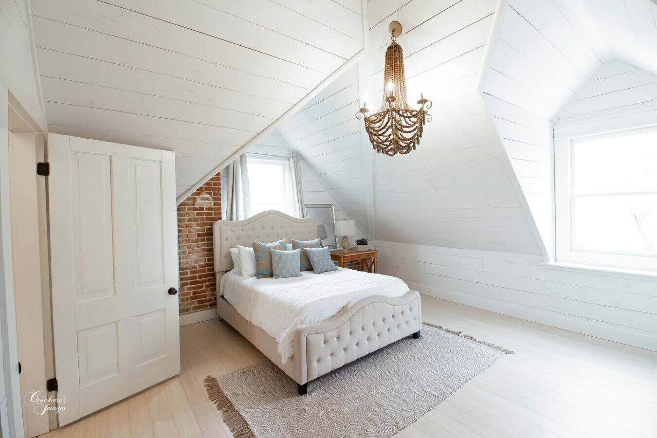 Een slaapkamer met een wit bed, een kroonluchter, een bakstenen muur en een groot raam.