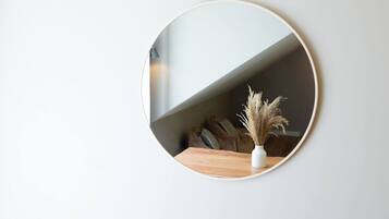 Un miroir rond accroché au mur, avec une table en bois en dessous, un vase contenant des plantes séchées et un canapé avec des coussins à l’arrière-plan.