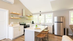 A modern kitchen with white cabinetry, a stainless steel refrigerator, and a central island with bar stools. - The Cottage, Rusted Route Farms (Jackson)