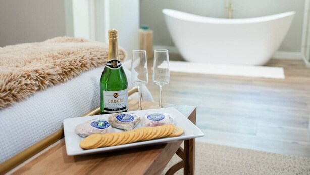 A bedroom with a bed, a bottle of J. Roget champagne, two glasses, and a plate with snacks. - The Cottage, Rusted Route Farms (Jackson)