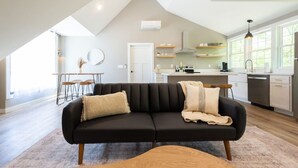 A modern living room with a black sofa, wooden coffee table, and a kitchen in the background. - The Cottage, Rusted Route Farms (Jackson)