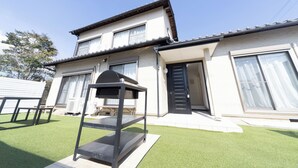 Una casa de dos pisos con balcón, patio y una pequeña parrilla al aire libre.