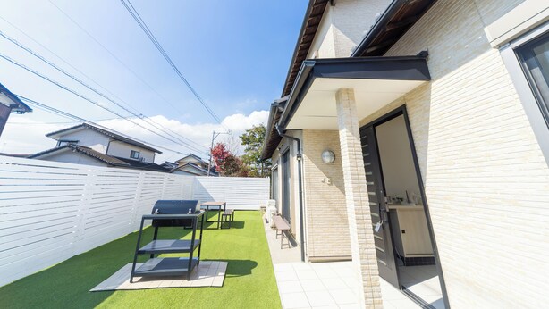 Un patio trasero residencial con césped artificial, una parrilla y una mesa de patio.