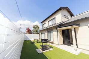 Una casa de dos pisos con un patio, una parrilla y una valla blanca.