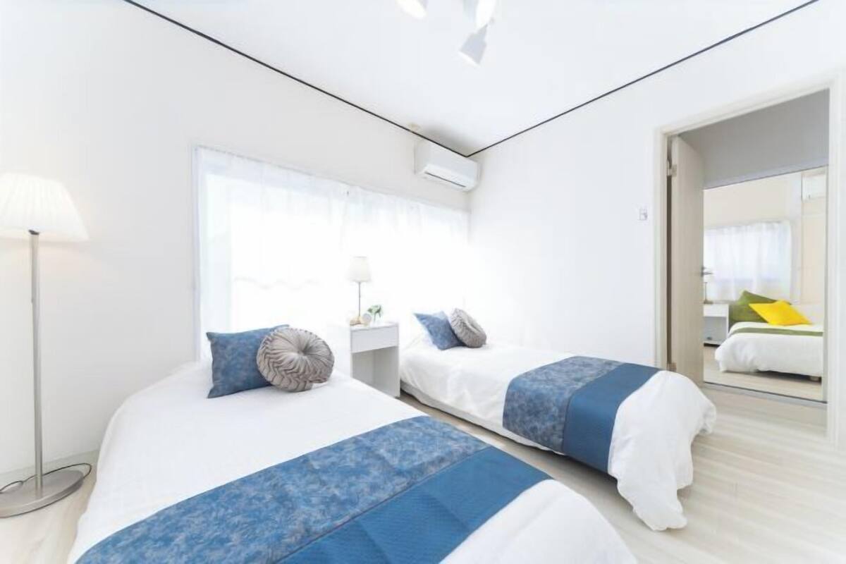 A modern hotel room with two beds, a bedside table, a lamp, and a large window.