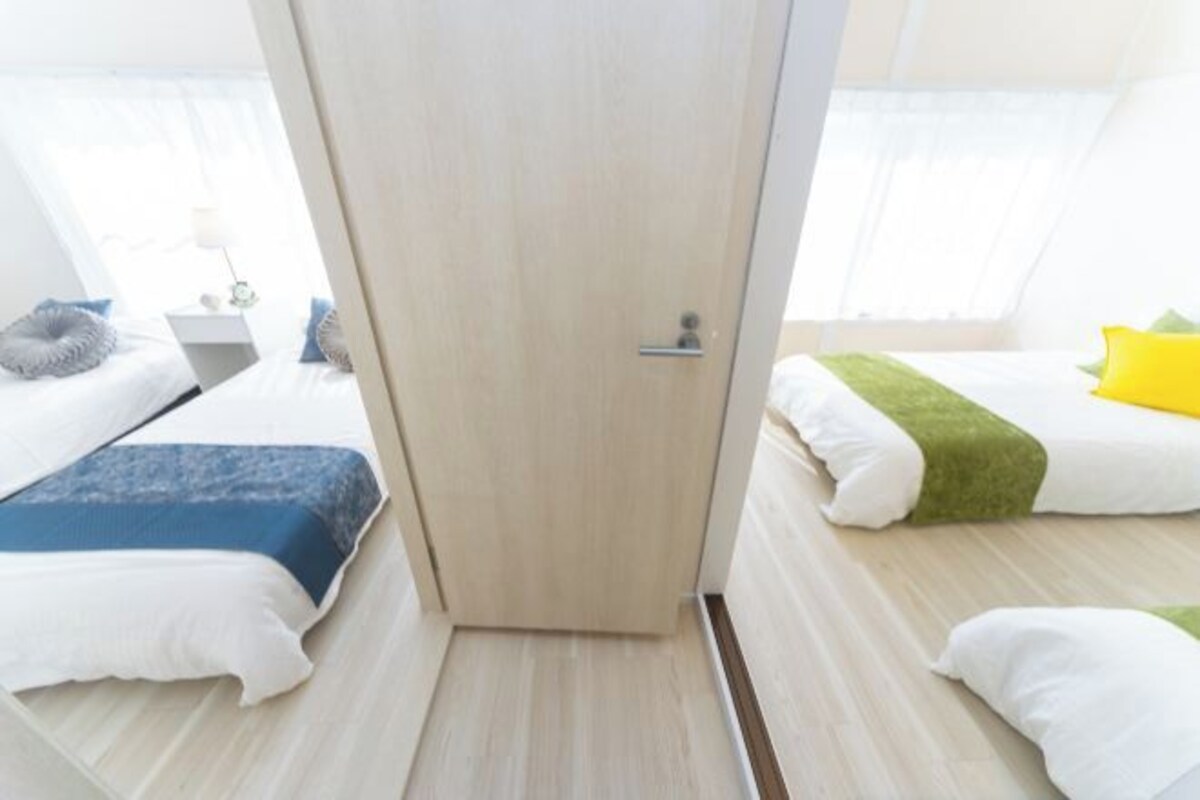 A hotel room with two beds, a wooden door, and a bedside table with a lamp.