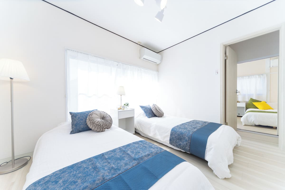 Habitación de hotel con dos camas, una mesita de noche, una lámpara y una ventana.