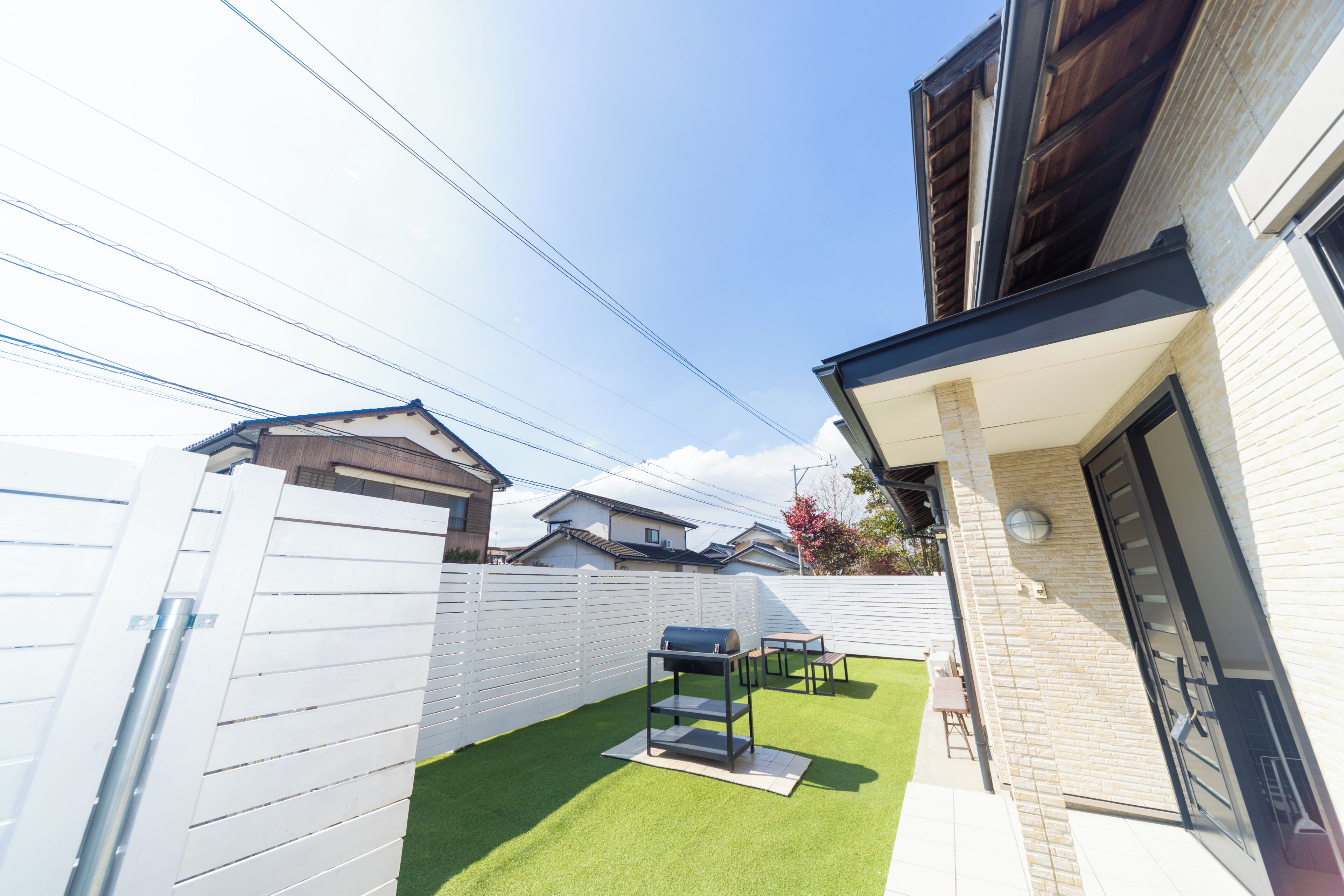A backyard with artificial grass, a barbecue grill, and a white fence.