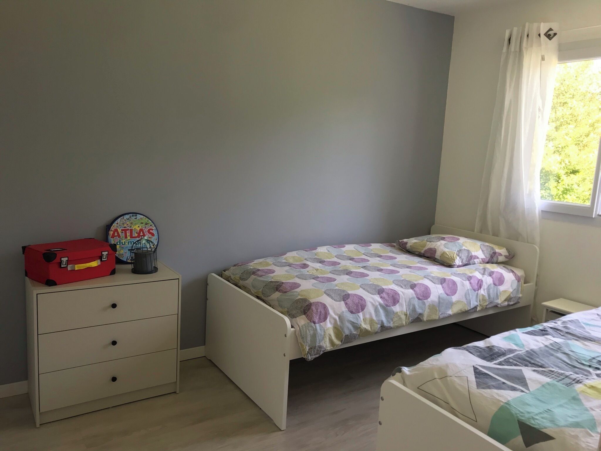 Een slaapkamer met een enkel bed, een nachtkastje, een dressoir en een raam met gordijnen.