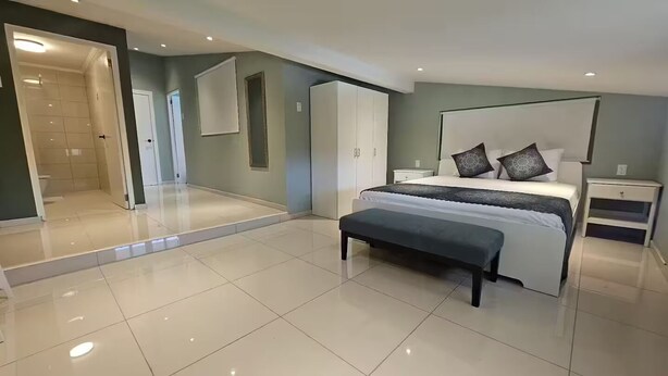 Een moderne slaapkamer met een groot bed, een bankje, een garderobe en een inloopkast.