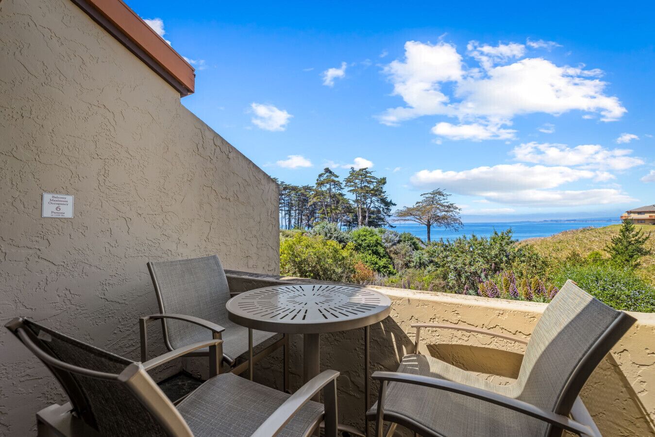 Une terrasse avec une table ronde et quatre chaises, offrant une vue panoramique sur l’océan et la forêt.
