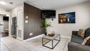 Un salon moderne avec un téléviseur à écran plat, un canapé, une table basse et une plante en pot.