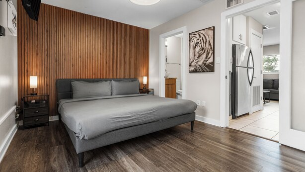 Une chambre moderne avec un grand lit, un mur recouvert de panneaux en bois et un réfrigérateur dans la pièce adjacente.