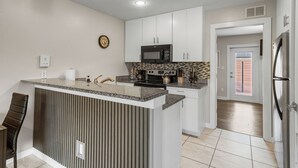 Une cuisine moderne dotée d’un îlot central, de meubles blancs, d’un four à micro-ondes et d’un réfrigérateur en acier inoxydable.