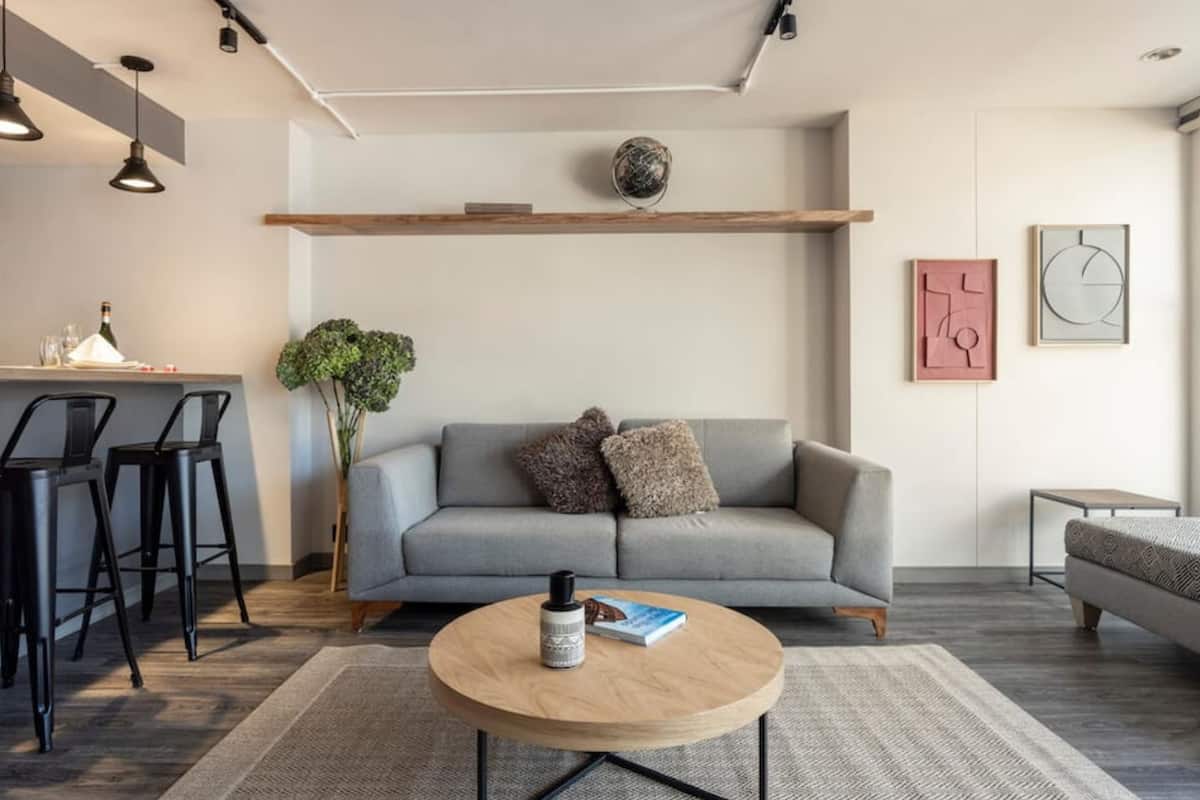 Un salon moderne avec un canapé gris, une table basse ronde et un coin repas équipé de tabourets de bar.