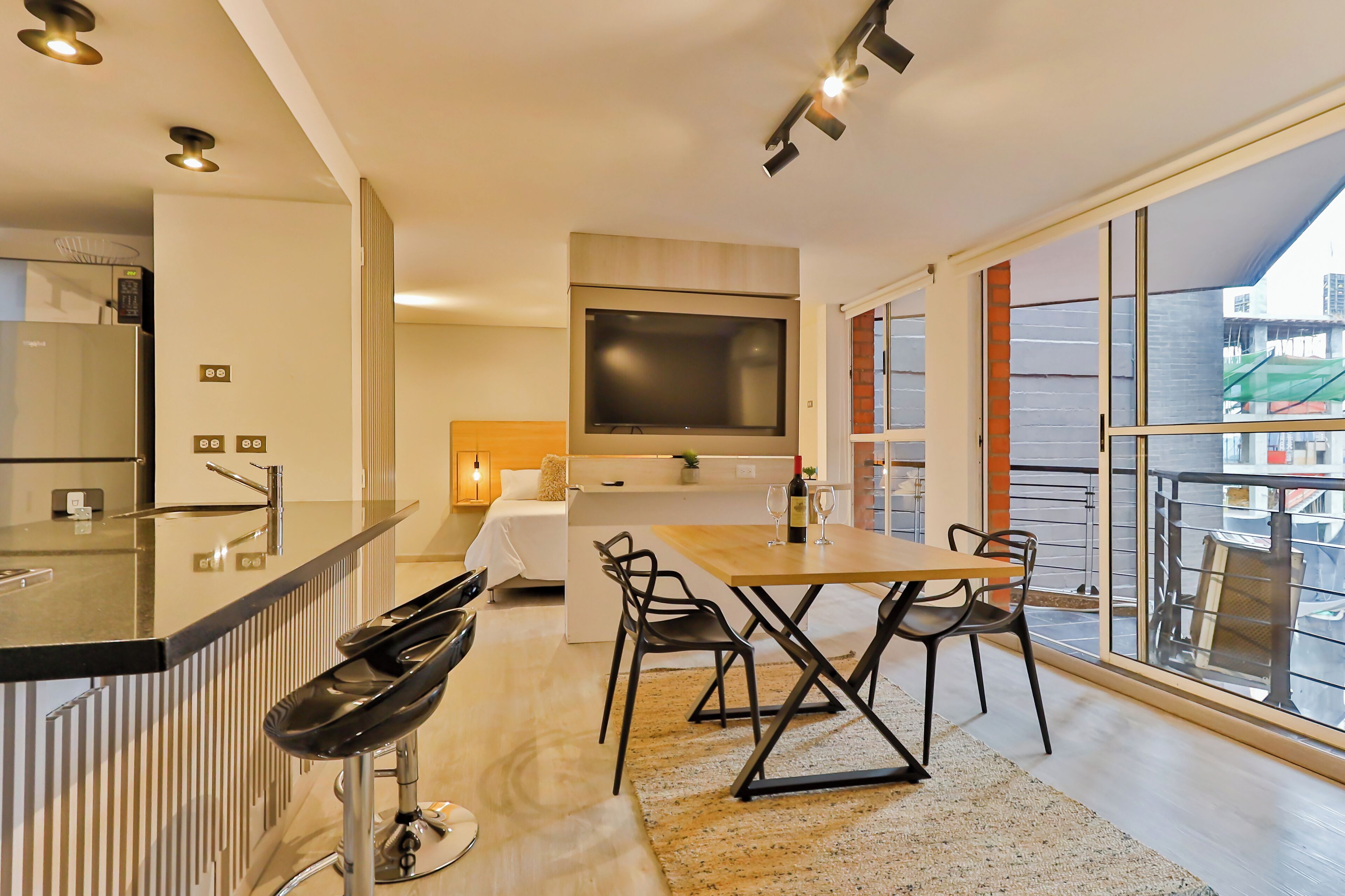 A modern kitchen with a large island, a dining area with a wooden table and chairs, and a large window offering a view of the city.