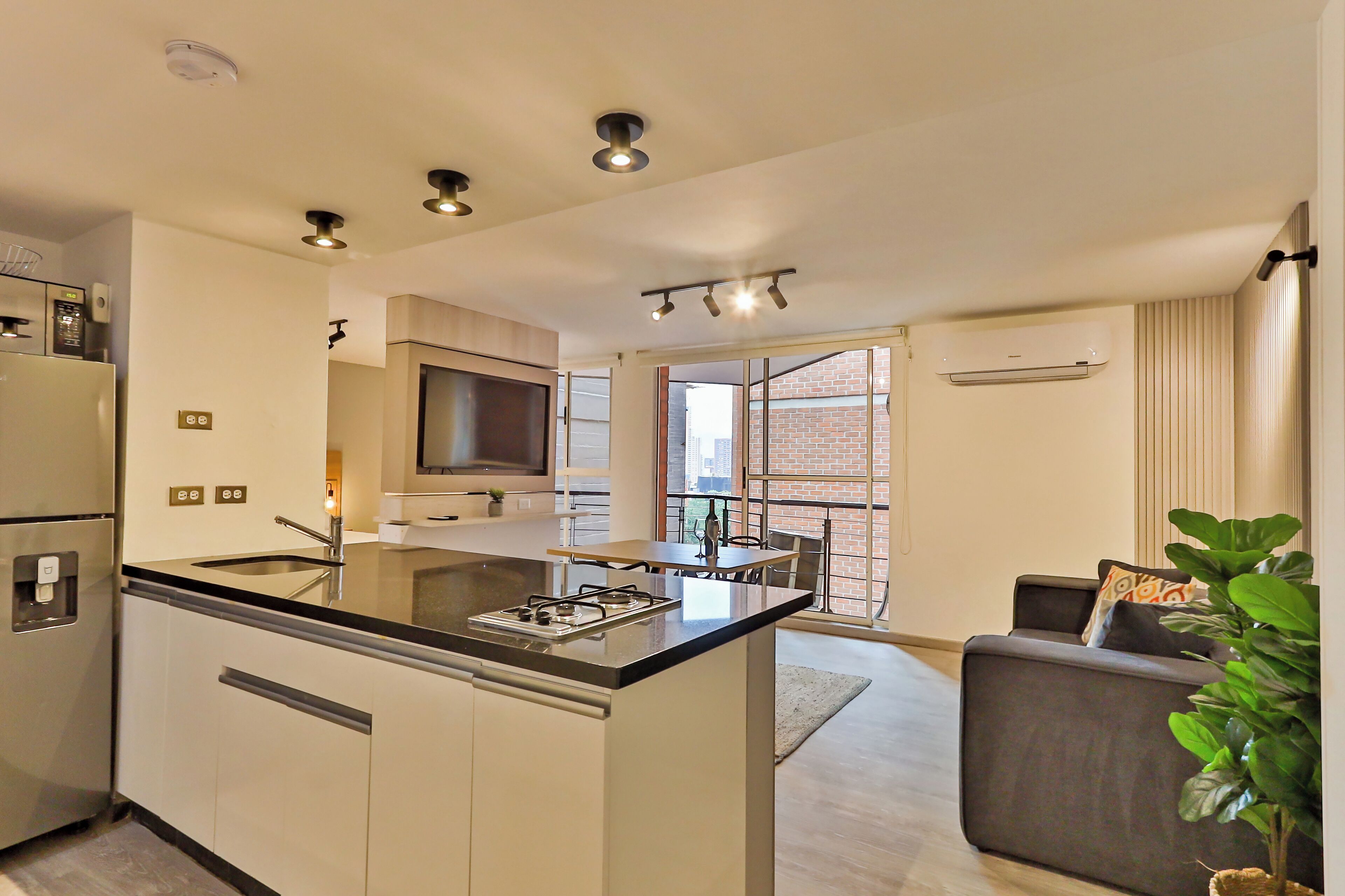 A modern kitchen with a central island, built-in appliances, and a dining area with a sofa and a plant.