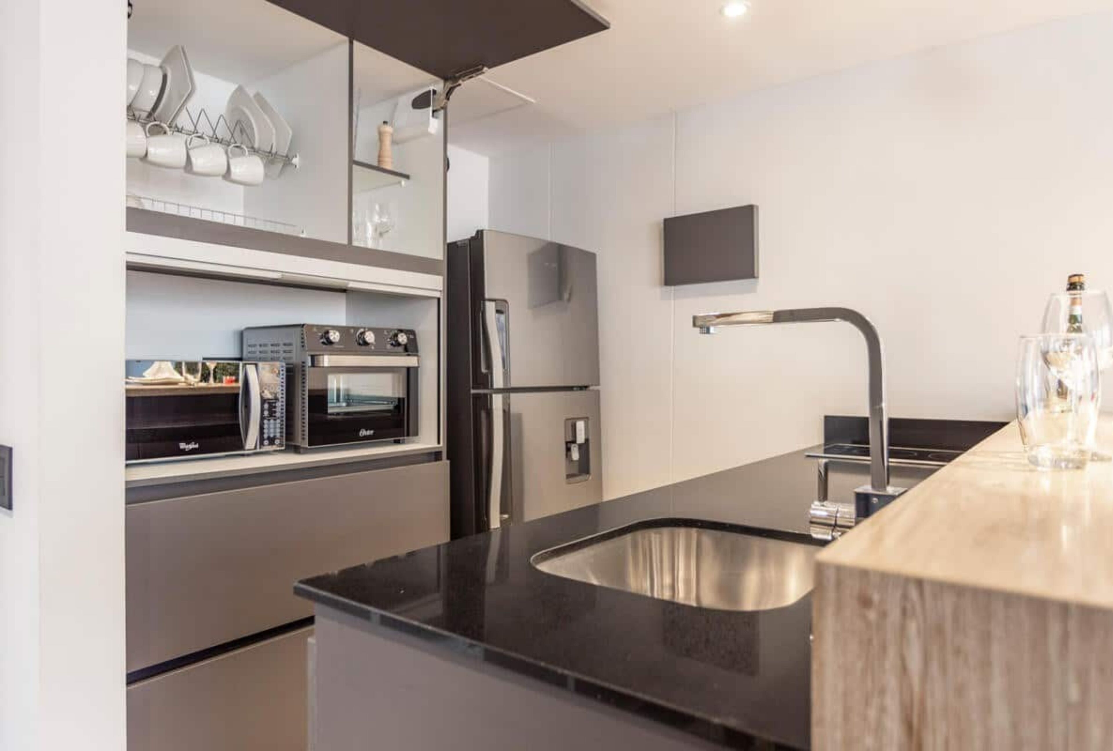 A modern kitchen with stainless steel appliances, a black countertop, and a built-in sink.