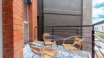 A balcony with a metal railing, two wicker chairs, a round table, and a patterned floor.