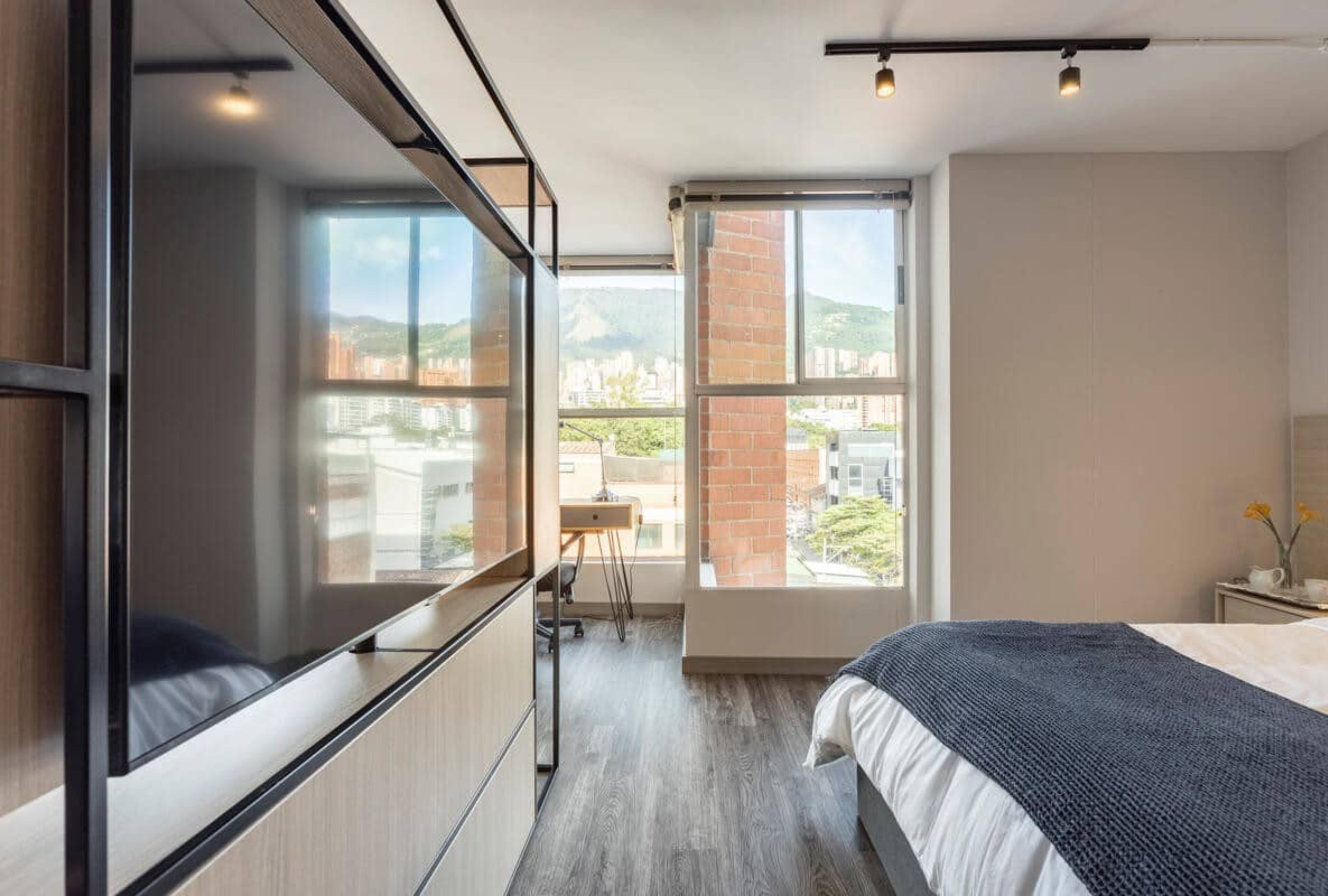 Een moderne slaapkamer met een groot bed, een bureau en uitzicht op de stad door grote ramen.