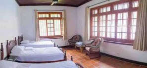 A room with two single beds, a chair, a small table, and large windows with curtains. - A Family Estate for the Perfect Vacation   (Parrita)