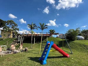A playground with a slide and swings, a staircase leading to a house, and a parked car. - Naldinho's Farm   (Mairinque)