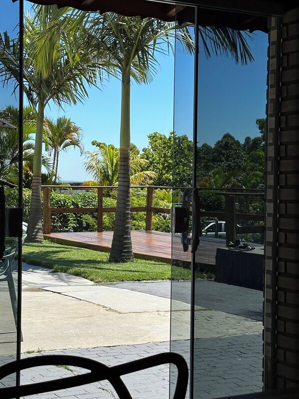 A view through a glass door of a patio area with palm trees, a wooden deck, and a brick wall.