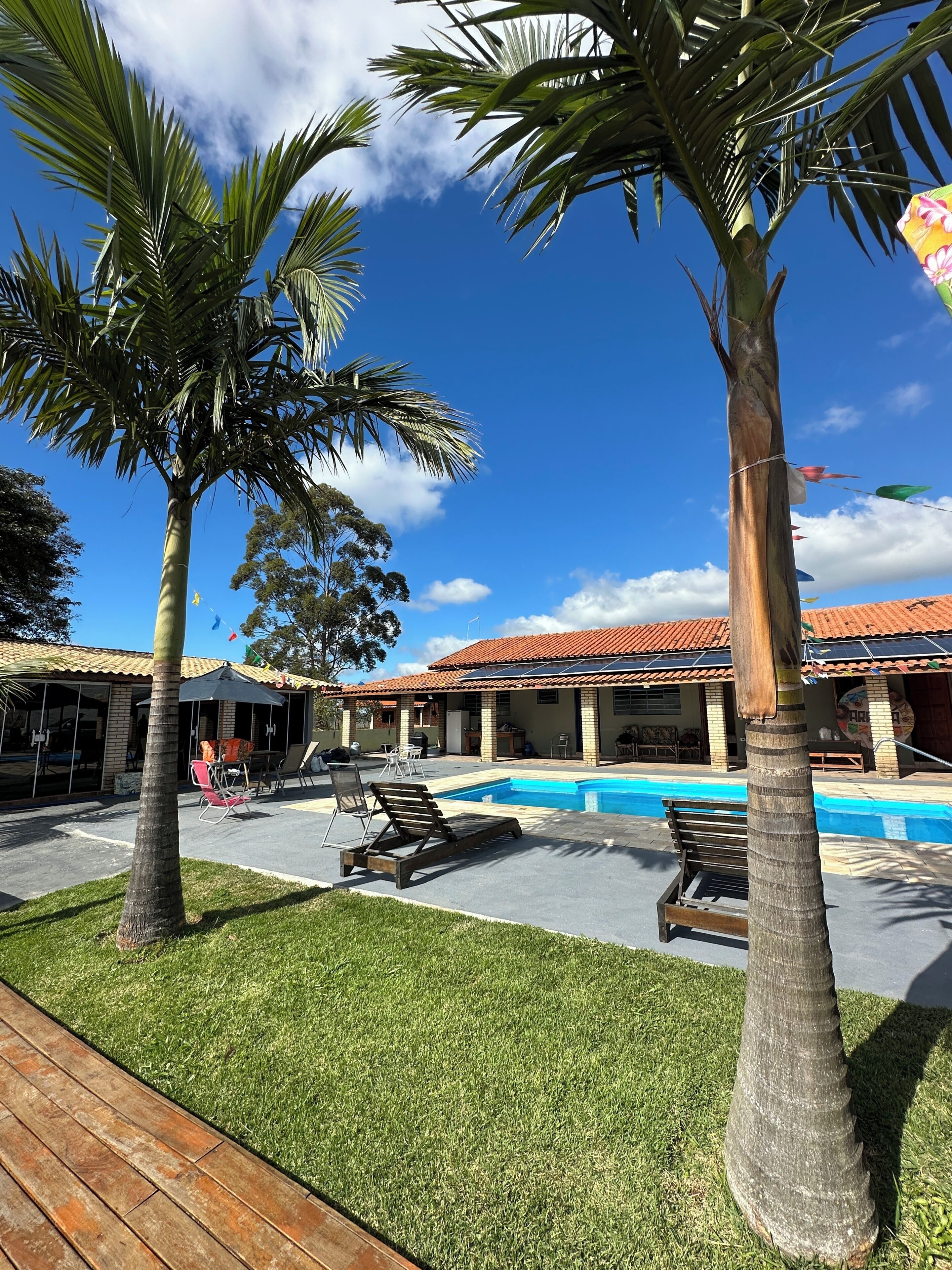 A pool area with lounge chairs, palm trees, and a building with a tiled roof.