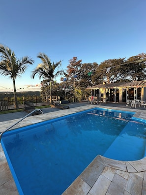 A swimming pool with a tiled deck, surrounded by palm trees and a covered patio area. - Naldinho's Farm (Mairinque)