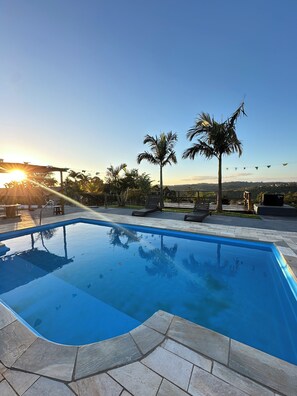 A swimming pool with a stone border, surrounded by palm trees and a clear sky.