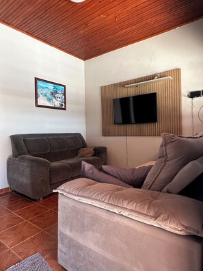A living room with a sofa, a television mounted on a wooden panel, and a framed picture on the wall.