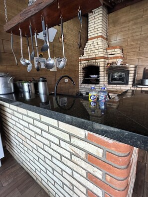 A kitchen with a brick oven, hanging utensils, and stainless steel cookware. - Naldinho's Farm   (Mairinque)