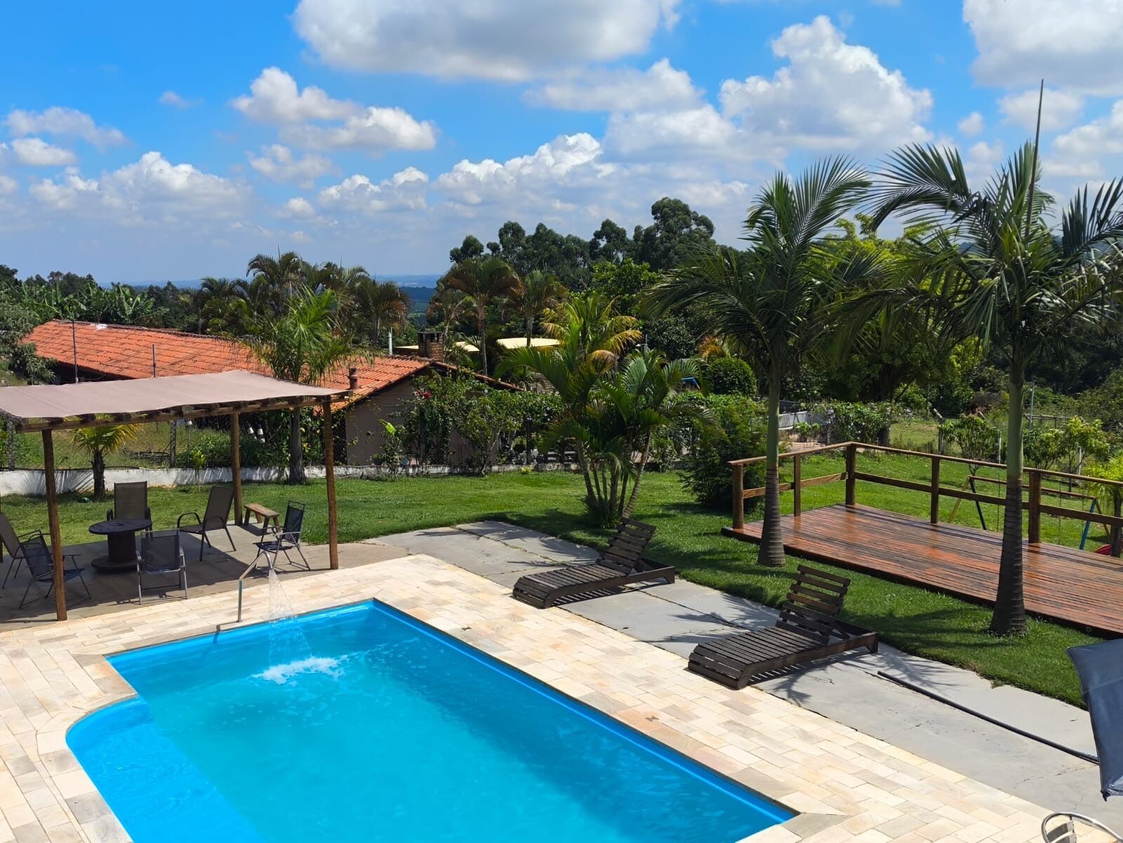 Une piscine avec une terrasse carrelée, un espace salon couvert et une terrasse en bois équipée de chaises longues.