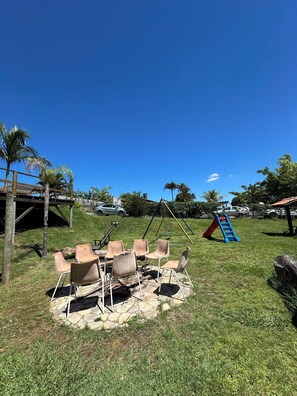 A grassy outdoor area with a swing set, a slide, and a seating area with chairs. - Naldinho's Farm (Mairinque)