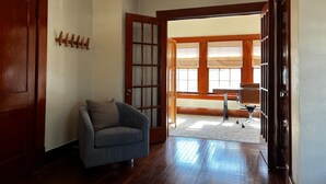 A room with a wooden floor, a grey armchair, and a wooden door with glass panels. - Montrose Home walkable neighborhood | Pet-friendly (Houston)