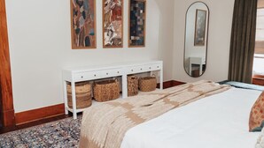 A bedroom with a bed, a white console table with baskets, a large mirror, and abstract art on the wall. - Montrose Home walkable neighborhood | Pet-friendly (Houston)