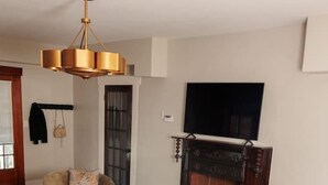 A living room with a brown leather sofa, a round wooden coffee table, a beige armchair, and a television mounted above a fireplace. - Montrose Home walkable neighborhood | Pet-friendly (Houston)