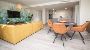 Un salon moderne avec un canapé jaune, une table à manger et des chaises, et une cuisine en arrière-plan.