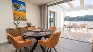 Un espace repas comprenant une table ronde, des chaises et une vue sur un plan d’eau et des collines.