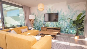 Ein Wohnzimmer mit einer Couch, einem Couchtisch, einem Fernseher und tropischem Wandpapier.