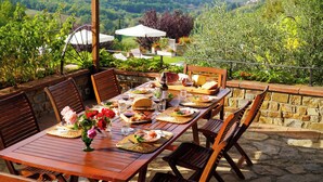 Un área de comedor al aire libre con una mesa preparada para una comida, rodeada de sillas y una pared de piedra.