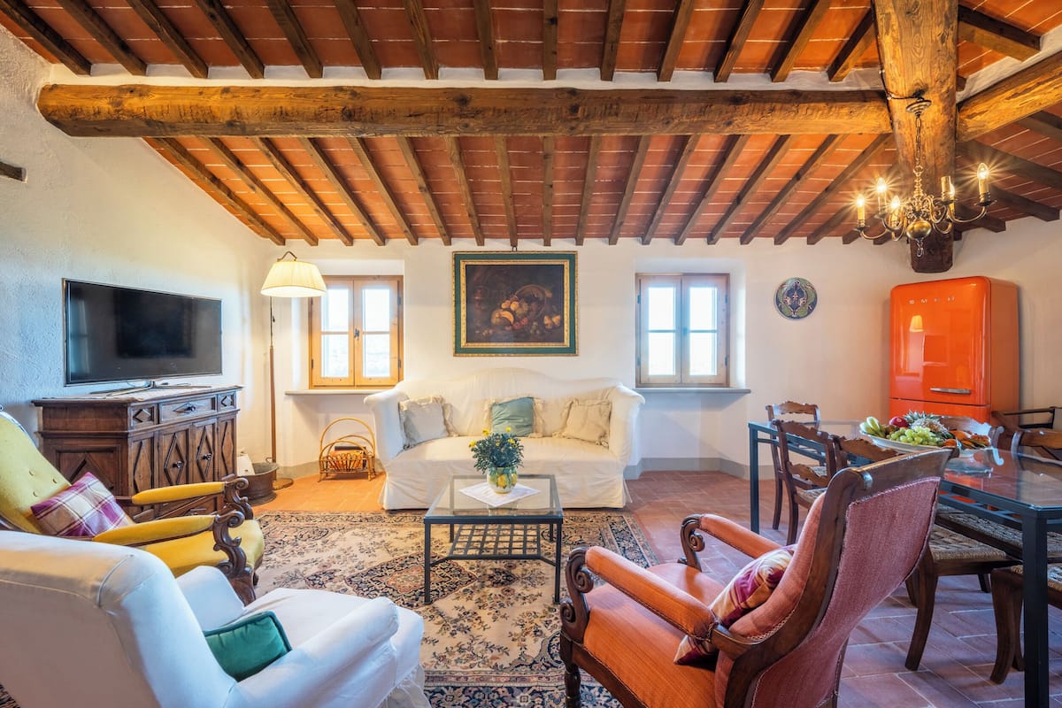 A cozy living room with a wooden ceiling, a television, a sofa, a coffee table, and a dining area with chairs and a table.