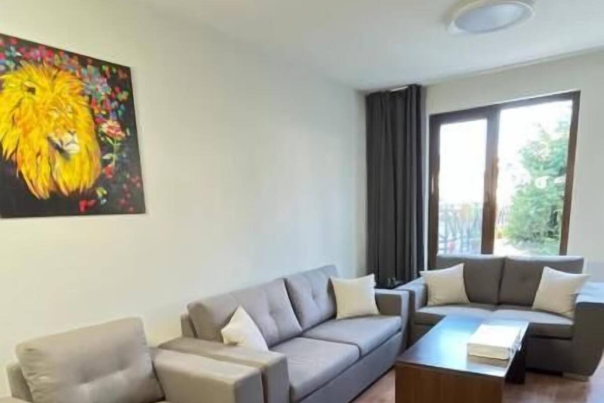 Ein modernes Wohnzimmer mit einem grauen Ecksofa, einem Holztisch und einem großen Fenster, das für natürliches Licht sorgt.