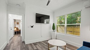 A modern living room with a round white table, a blue sofa, and a large window with blinds. - The Heights Collective (Tampa)