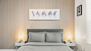A bedroom with a bed, two bedside tables with lamps, a wall-mounted artwork, and a window with blinds. - The Heights Collective (Tampa)