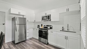 A modern kitchen with white cabinets, stainless steel appliances, and a wooden floor. - The Heights Collective (Tampa)