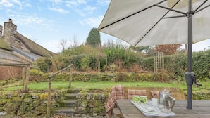 A rustic outdoor seating area with a wooden table, a bench, and a large umbrella.