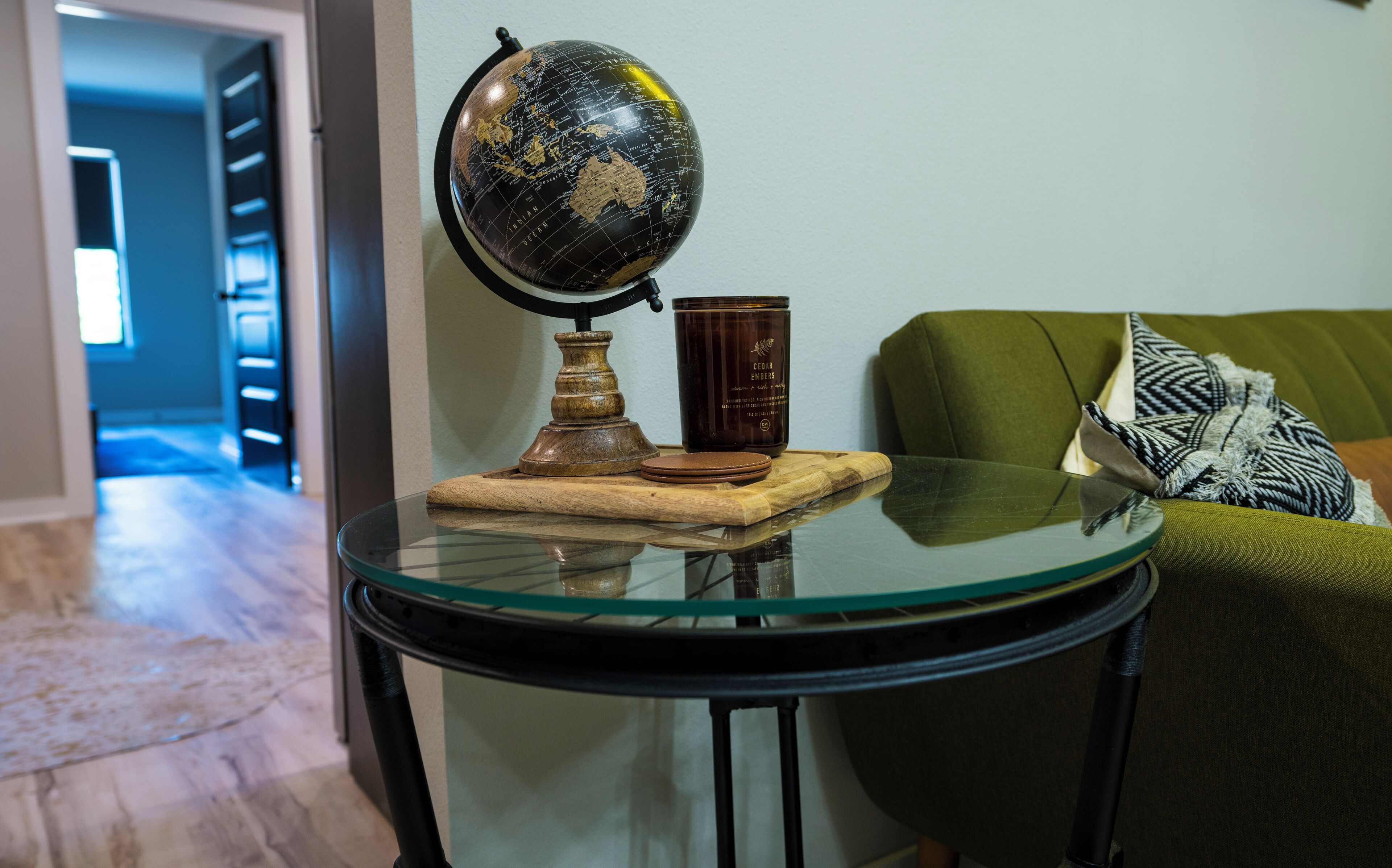 Una mesa redonda de cristal con un globo terráqueo, una vela y una bandeja de madera.